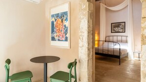 Une pièce comprenant un lit, une table, deux chaises et un tableau accroché au mur.