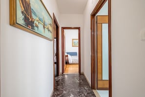 A hallway with a marble floor, wooden doors, and a bed with a blue headboard in the background.