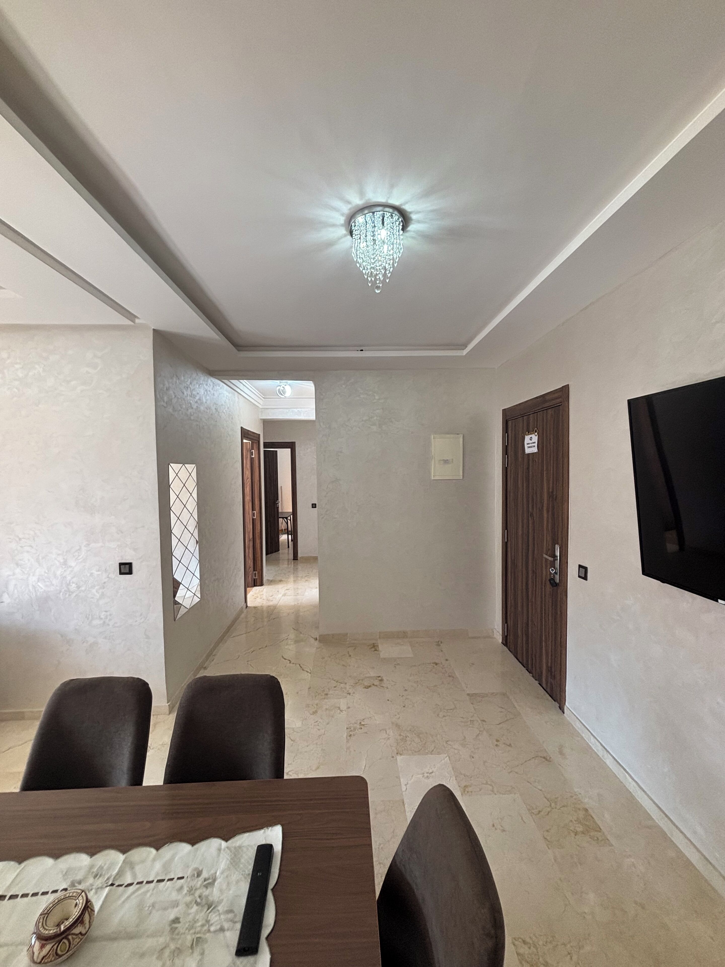 Une chambre d’hôtel avec un coin repas, un lustre, un téléviseur fixé au mur et une porte avec une pancarte.