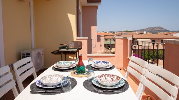 A dining table set on a balcony with a clear view of the cityscape and mountains in the distance.