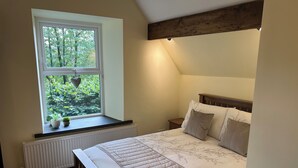 Ein Schlafzimmer mit einem großen Bett, einem Fenster mit Blick auf Grünflächen, einem Heizkörper und einem Holzkopfende.