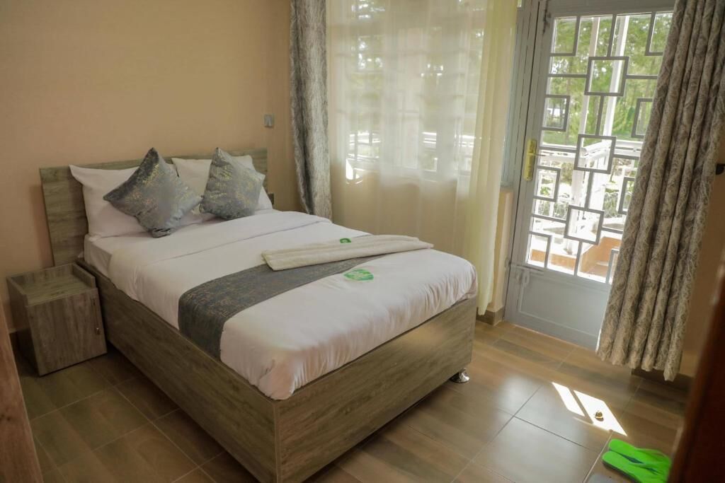 A bedroom with a wooden bed, a nightstand, and a view through a window with a geometric pattern.