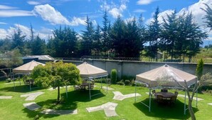 Un jardin avec trois tables de pique-nique abritées, un sentier en pierre et une vue sur une zone boisée.