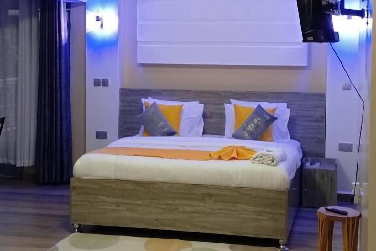 Une chambre moderne avec un grand lit, un téléviseur à écran plat fixé au mur et un luminaire au plafond.