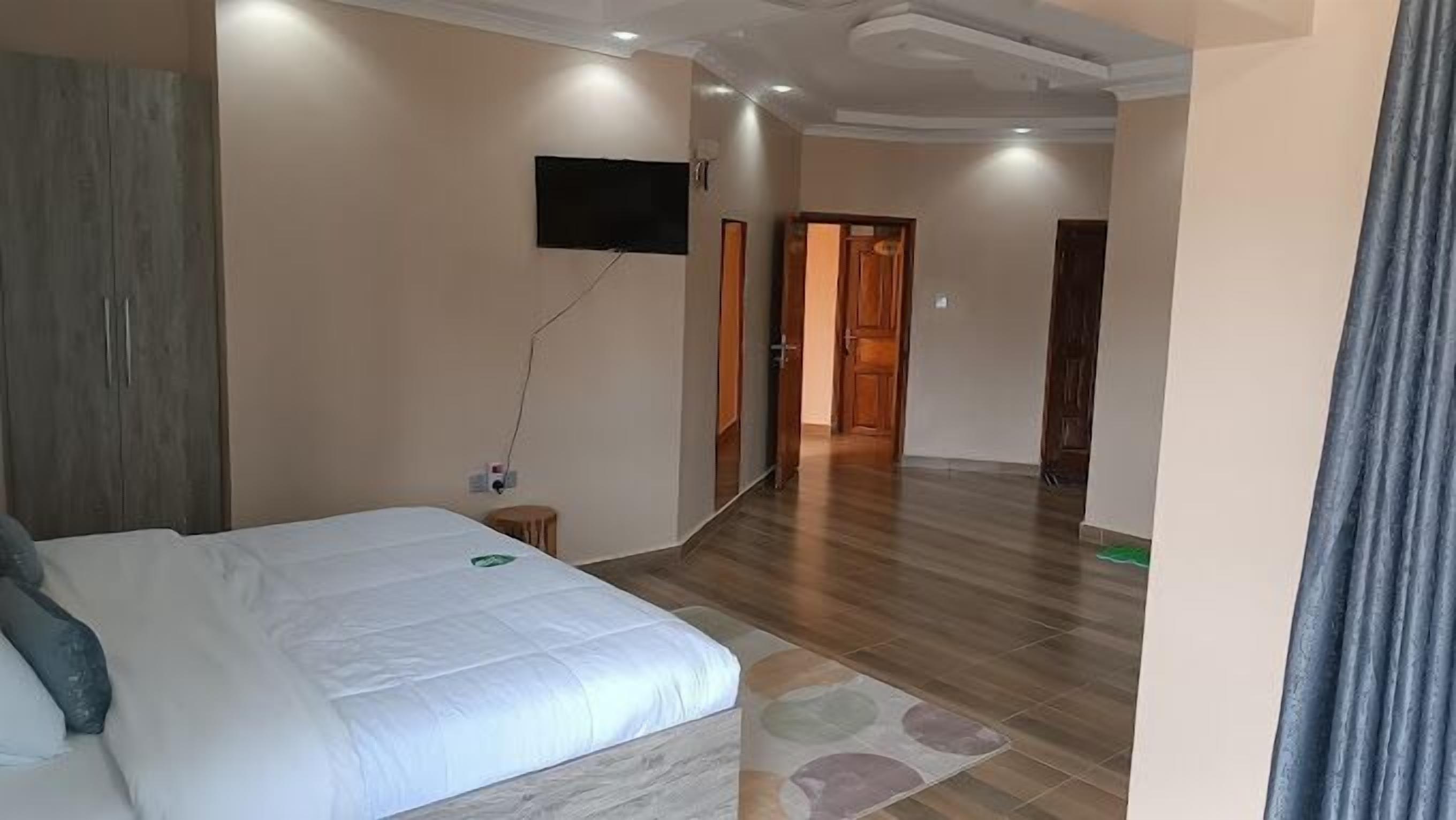 Un dormitorio con una cama, un televisor instalado en la pared y un pasillo que conduce a otra habitación.