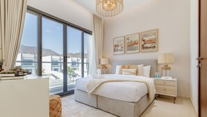 Un dormitorio moderno con una cama grande, dos mesitas de noche, una lámpara de noche, un ventanal con cortinas y una obra de arte en la pared.