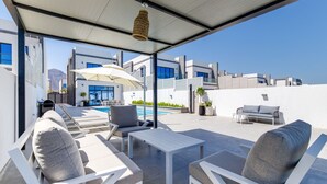 Un área de descanso al aire libre, moderna, con mobiliario blanco, piscina y vistas despejadas de los edificios circundantes.