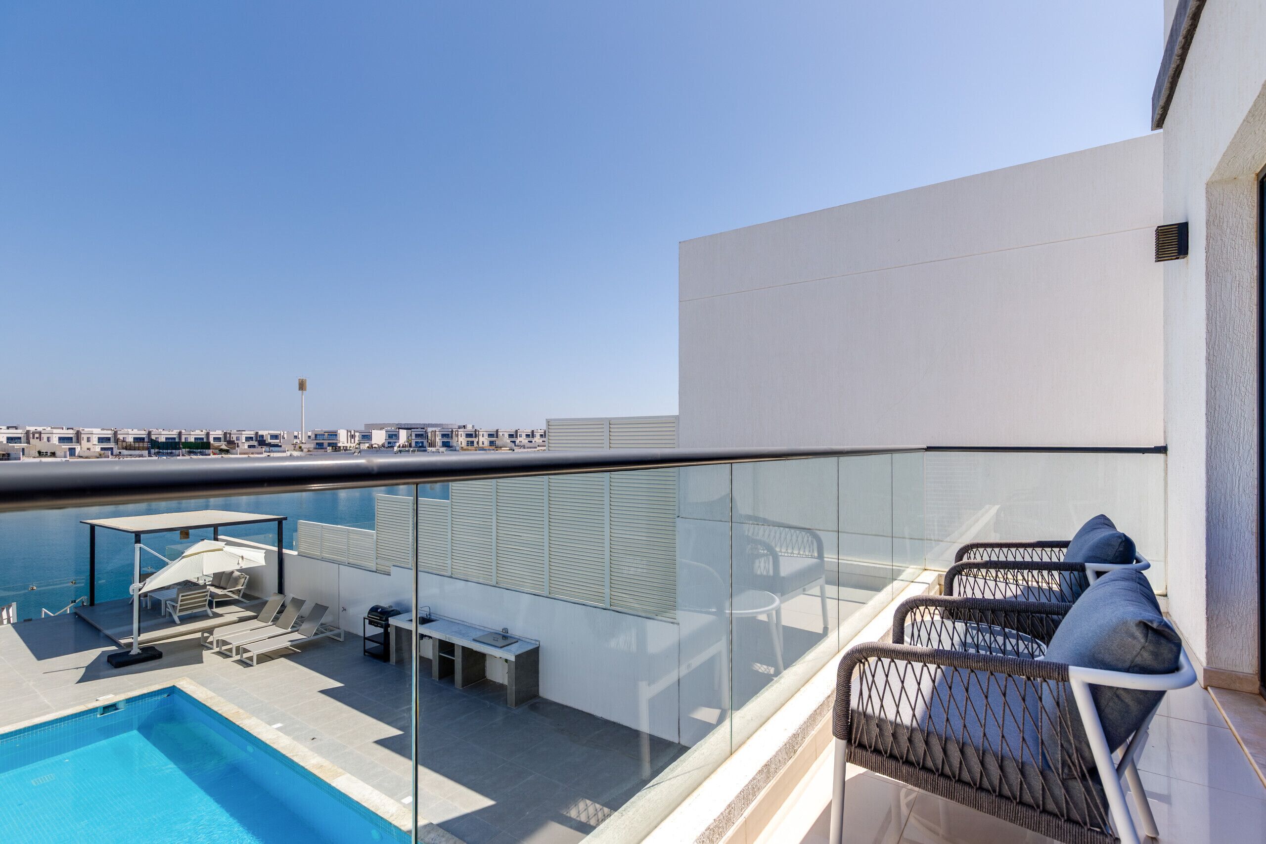A rooftop pool area with lounge chairs, a small table, and a glass balustrade.
