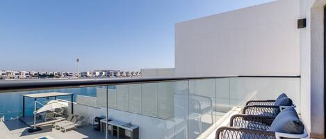 A rooftop pool area with lounge chairs, a small table, and a glass balustrade.