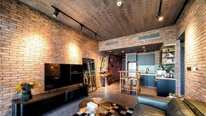 A modern living room with a brick wall, a round coffee table, a sofa, and a kitchen area in the background.