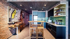 A modern kitchen with a brick wall, wooden stools, a central island, and a bookshelf with books.