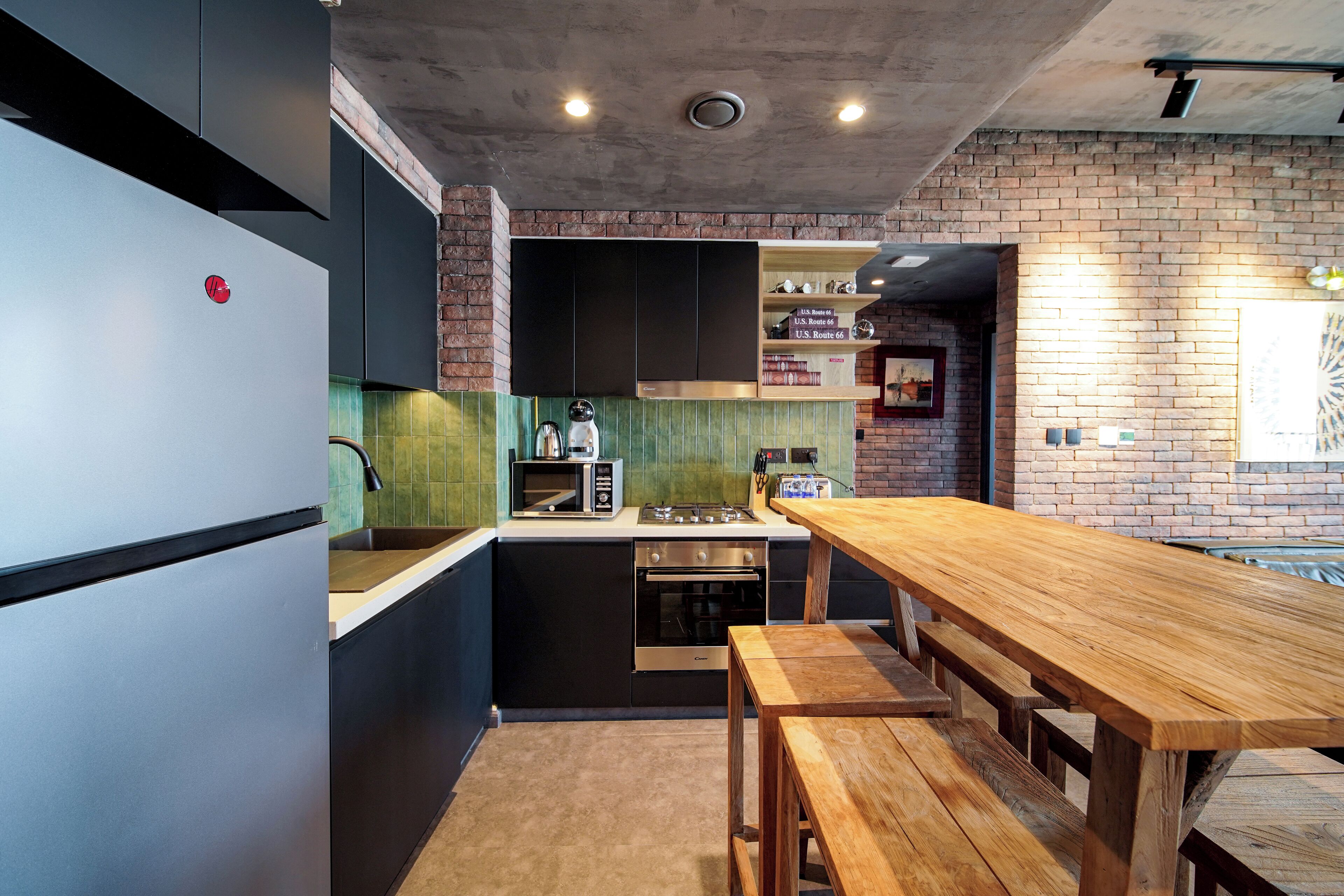 A modern kitchen with a wooden table and benches, built-in appliances, and a brick wall.