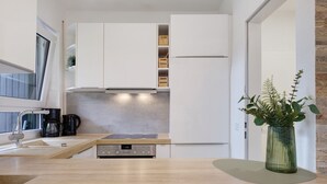 Een moderne keuken met witte kasten, een inbouwoven, een koffiezetapparaat en een plantje op het aanrecht.