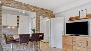 Een moderne keuken met een achterwand van steen, een eethoek met barstoelen, een flatscreen televisie en een houten kast.