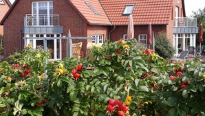 Ein zweistöckiges Haus mit rotem Ziegeldach, einem Balkon und einem Garten mit Obstbäumen.