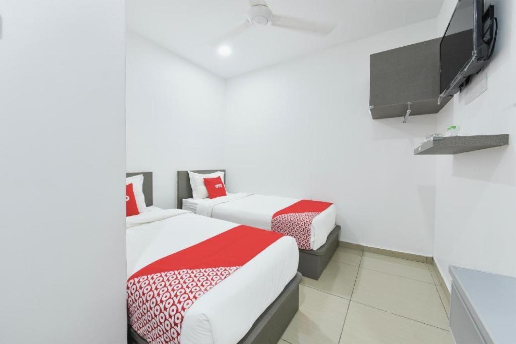 Una habitación de hotel con dos camas, un televisor montado en la pared y una pequeña estantería.