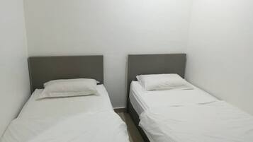 Two single beds with grey headboards in a room with plain white walls.