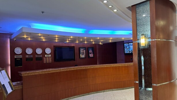 A reception area with a wooden counter, clocks displaying different time zones, and a flat-screen TV. - Mayon Hotel (Riyadh)