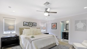 A bedroom with a bed, nightstand, lamp, ceiling fan, and artwork on the walls.