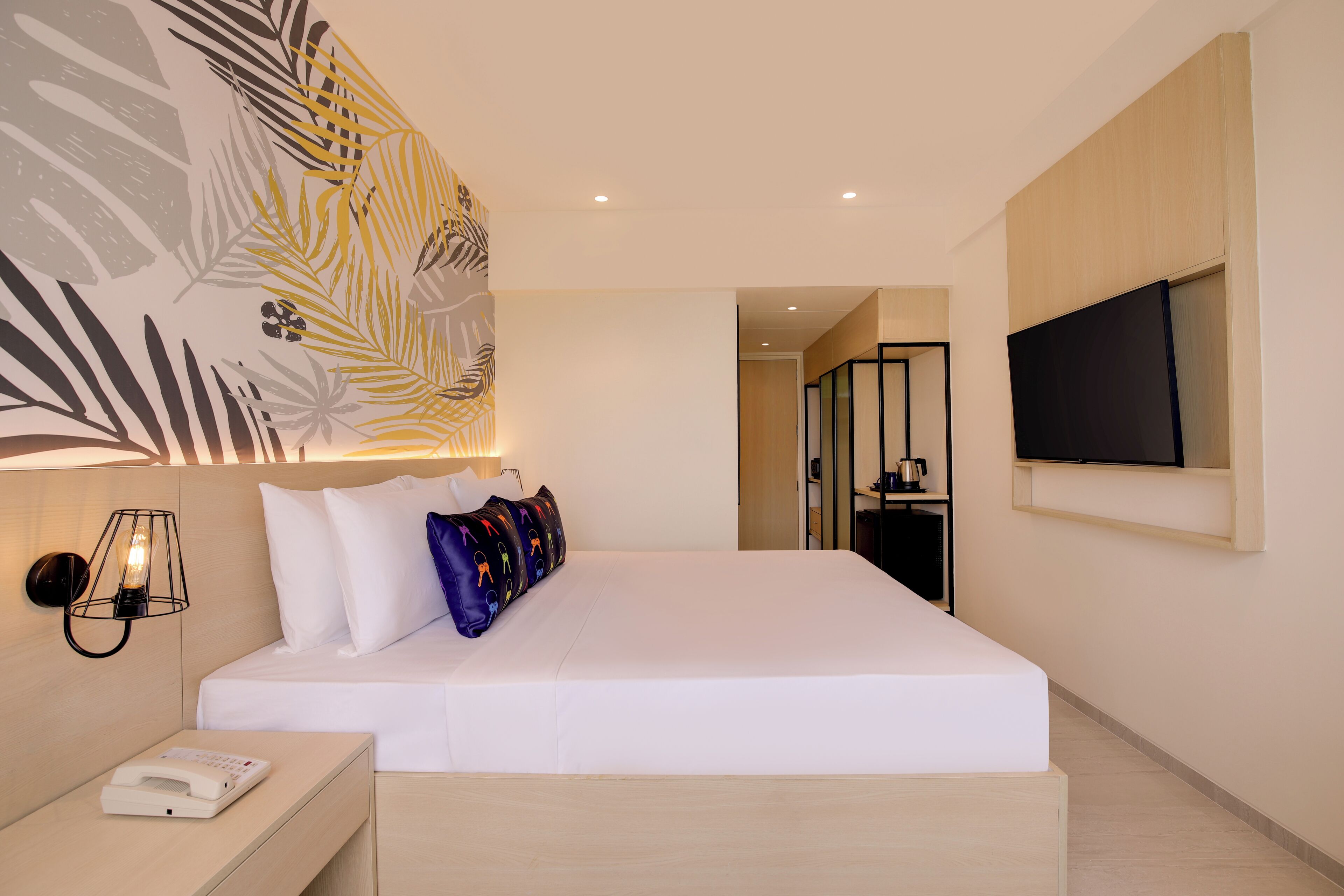 Quarto de hotel moderno com uma cama grande, telefone ao lado da cama, televisão presa à parede e uma obra de arte decorativa.