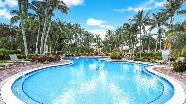 A large, clear swimming pool surrounded by palm trees and lounge chairs. - Bolero at Tiburon - First Floor Luxury Condo (Naples)