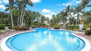 A large, clear swimming pool surrounded by palm trees and lounge chairs.