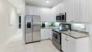 A modern kitchen with white cabinets, stainless steel appliances, and a granite countertop. - Bolero at Tiburon - First Floor Luxury Condo (Naples)