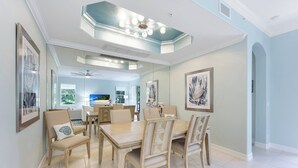 A spacious dining area with a high ceiling, modern lighting, and a view of the kitchen in the background. - Bolero at Tiburon - First Floor Luxury Condo (Naples)