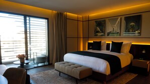 Une chambre d’hôtel moderne dotée d’un grand lit, d’un coin salon avec une table et des chaises, et d’œuvres d’art accrochées aux murs.