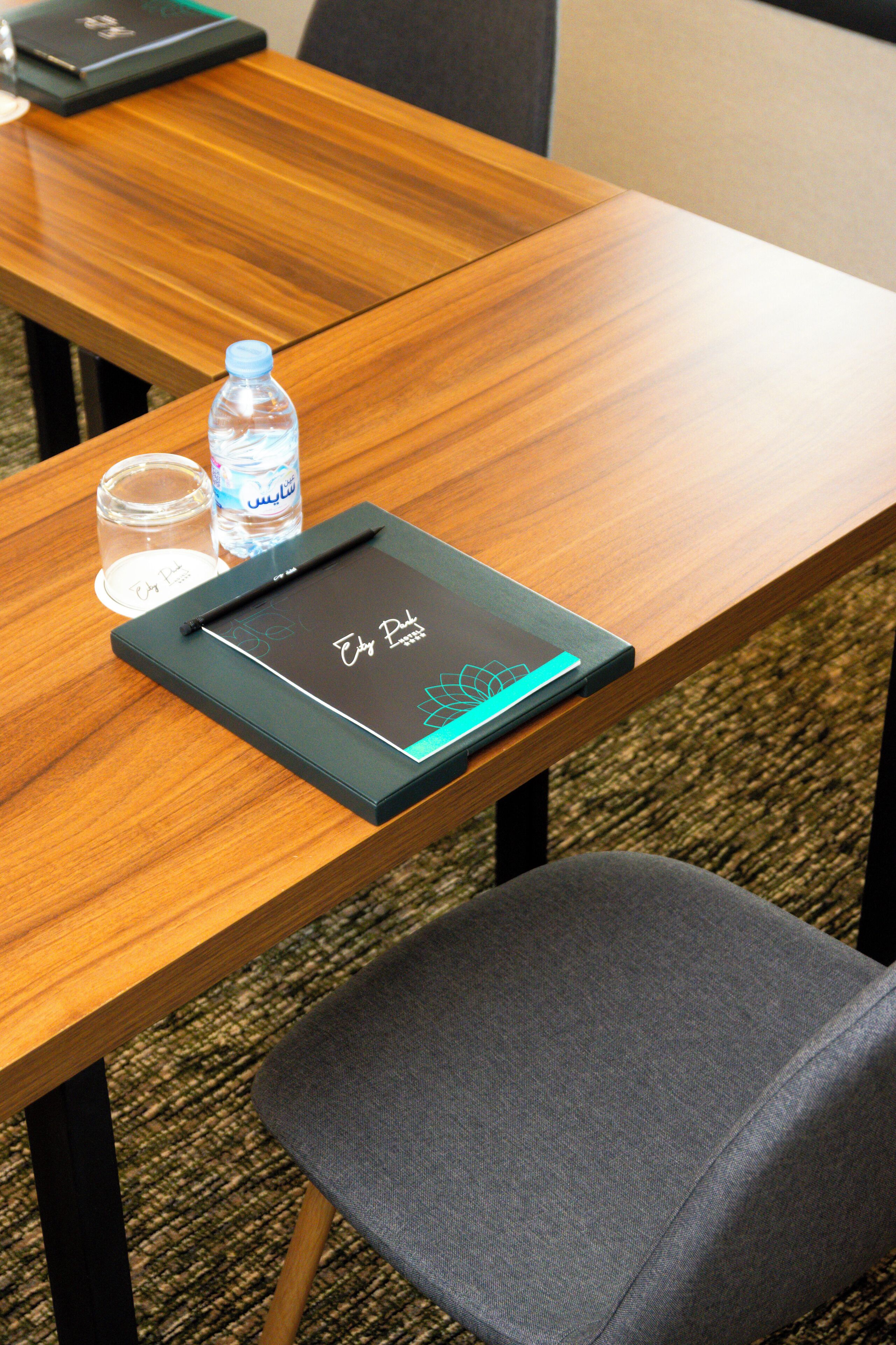Une table en bois avec un ordinateur portable, une bouteille d’eau et un verre.