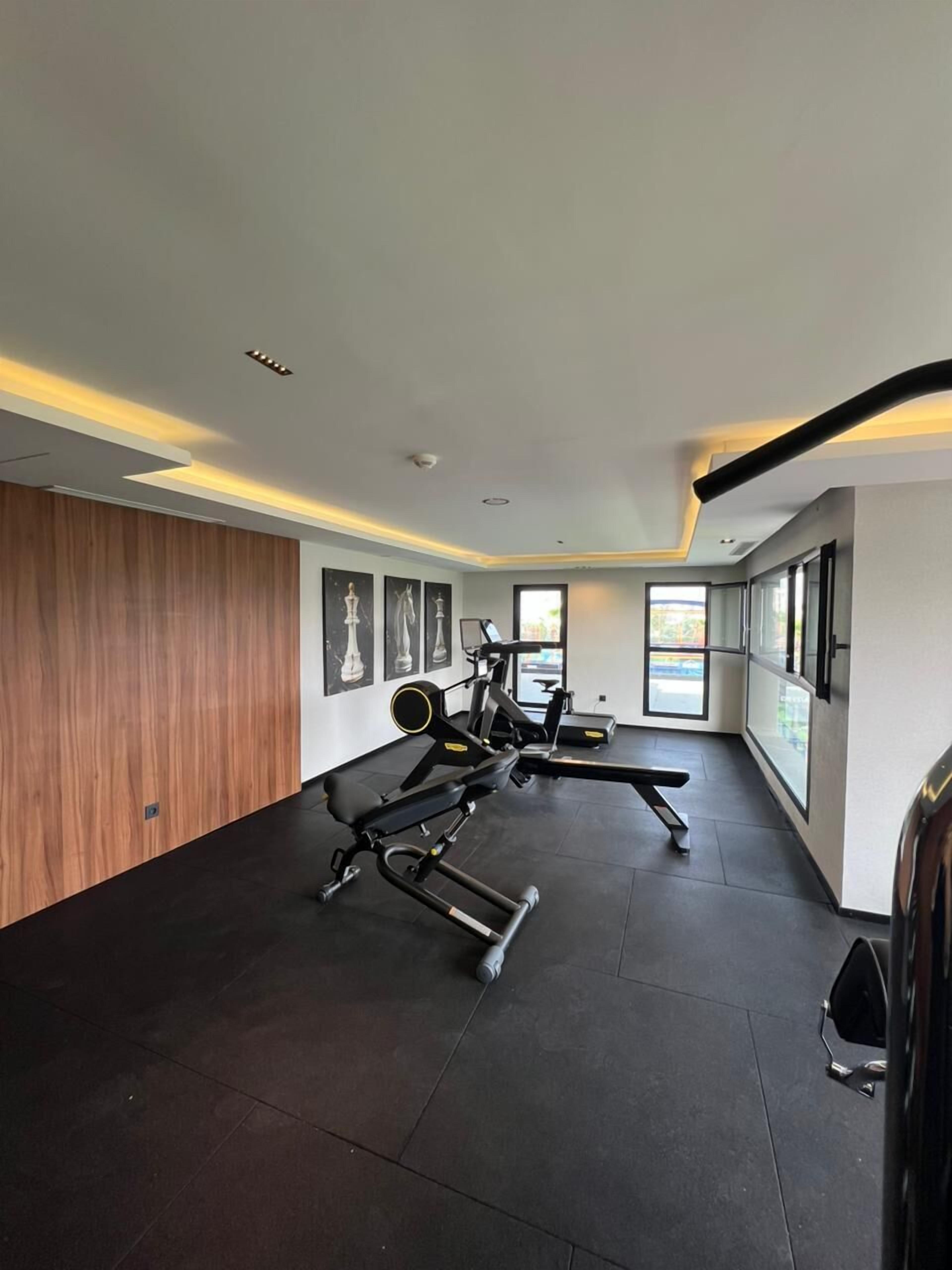 A modern gym with exercise equipment, large windows, and a wooden accent wall.