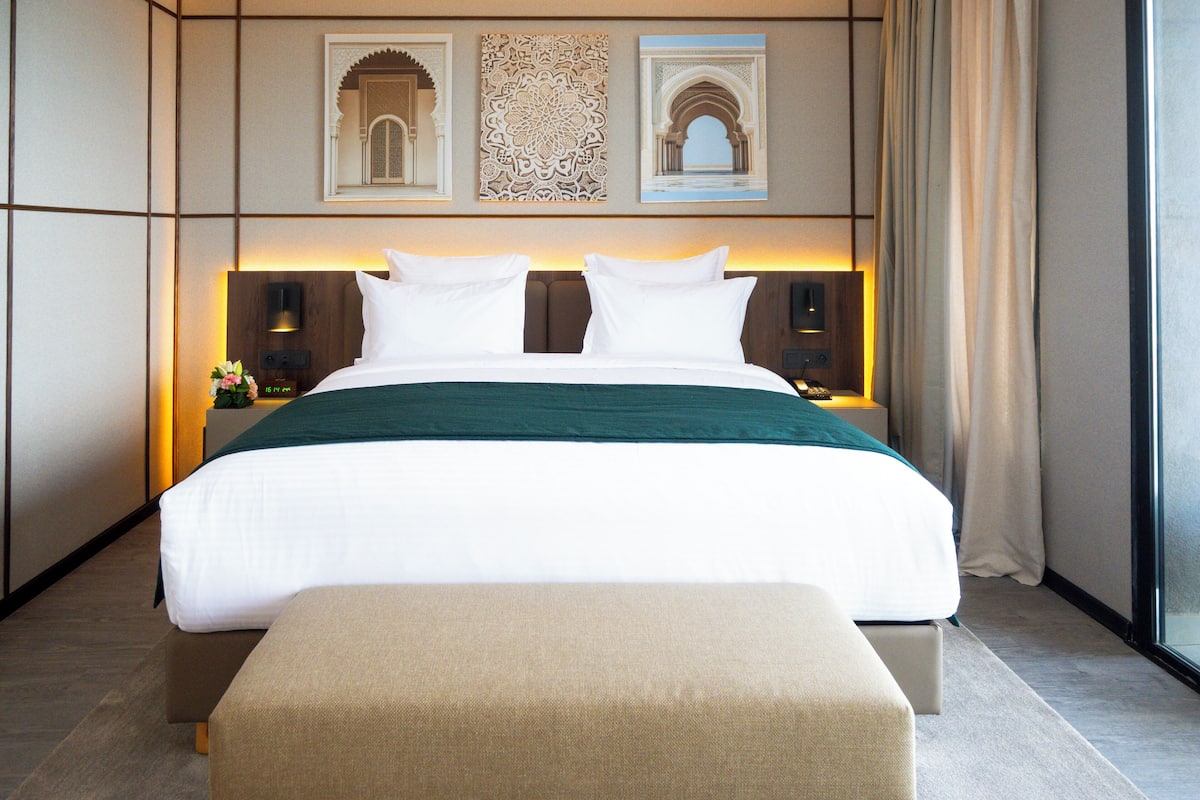A modern hotel room with a large bed, a bench, and decorative wall art.
