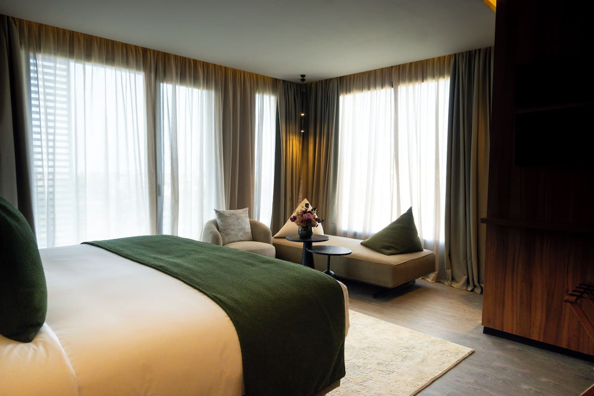 A hotel room with a large bed, a sofa, a small table with a vase, and curtains.