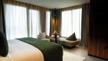 Habitación de hotel con una cama grande, un sofá, una pequeña mesa con un florero y un armario de madera.