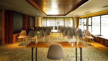 Un salón de conferencias con una larga mesa y varias sillas, ventanas amplias con cortinas y suelo alfombrado.