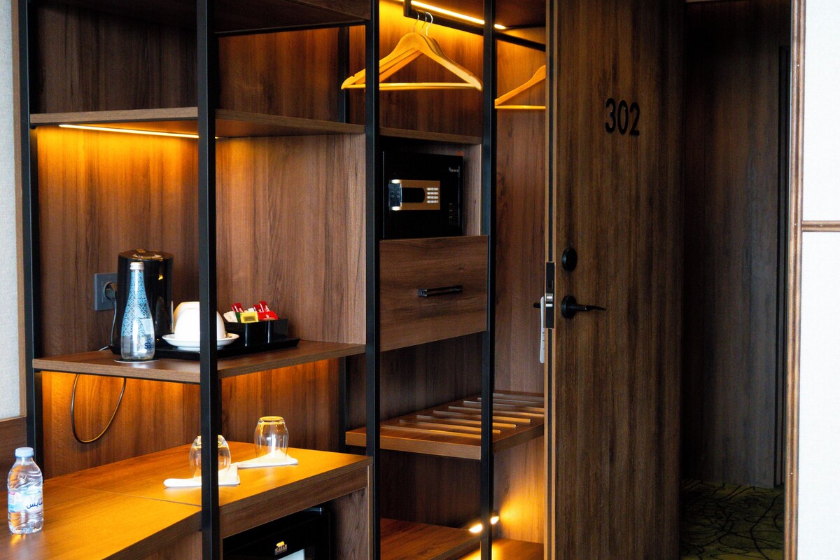 A compact hotel room with a built-in desk, a minibar, and a door marked with the number 302.