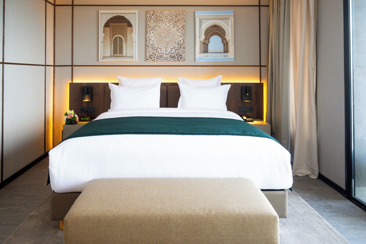 A modern hotel room with a large bed, a bench, and decorative wall art.