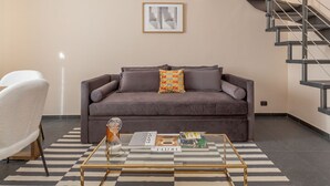Un salón con un sofá gris, una mesa de centro con revistas y una escalera a la derecha.