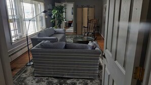 Een woonkamer met een grijze bank, een ronde salontafel en een kamerbreed tapijt met dessin.