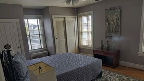 Een slaapkamer met een bed, een nachtkastje, een lamp, een dressoir en een raam met jaloezieën.