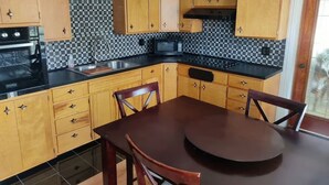 Een keuken met houten kastjes, een zwart fornuis, een magnetron en een ronde eettafel met stoelen.