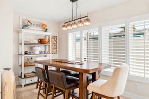 Un comedor con una mesa de madera, sillas, una araña y una ventana con persianas.