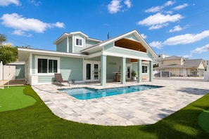 Una casa de dos pisos con piscina, un patio cubierto y un césped bien cuidado.