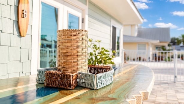 Wicker furniture on a wooden deck, a wooden surfboard with a logo, and a building with large windows.