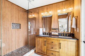 Un baño moderno con paneles de madera, cabina de ducha de vidrio, tocador con lavabo y un espejo grande.