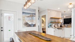 A modern kitchen with white cabinets, a wooden dining table, and a large painting on the wall.