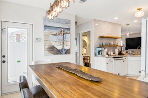 A modern kitchen with white cabinets, a wooden dining table, and a large painting on the wall.