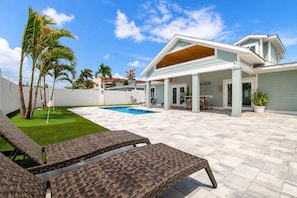 A modern house with a swimming pool, outdoor furniture, and palm trees.