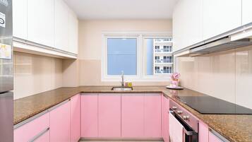 A kitchen with pink cabinets, a stainless steel refrigerator, a black stove, and a window with a view of buildings.