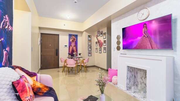 A modern living room with a flat-screen TV, a fireplace, and a dining area with pink chairs.